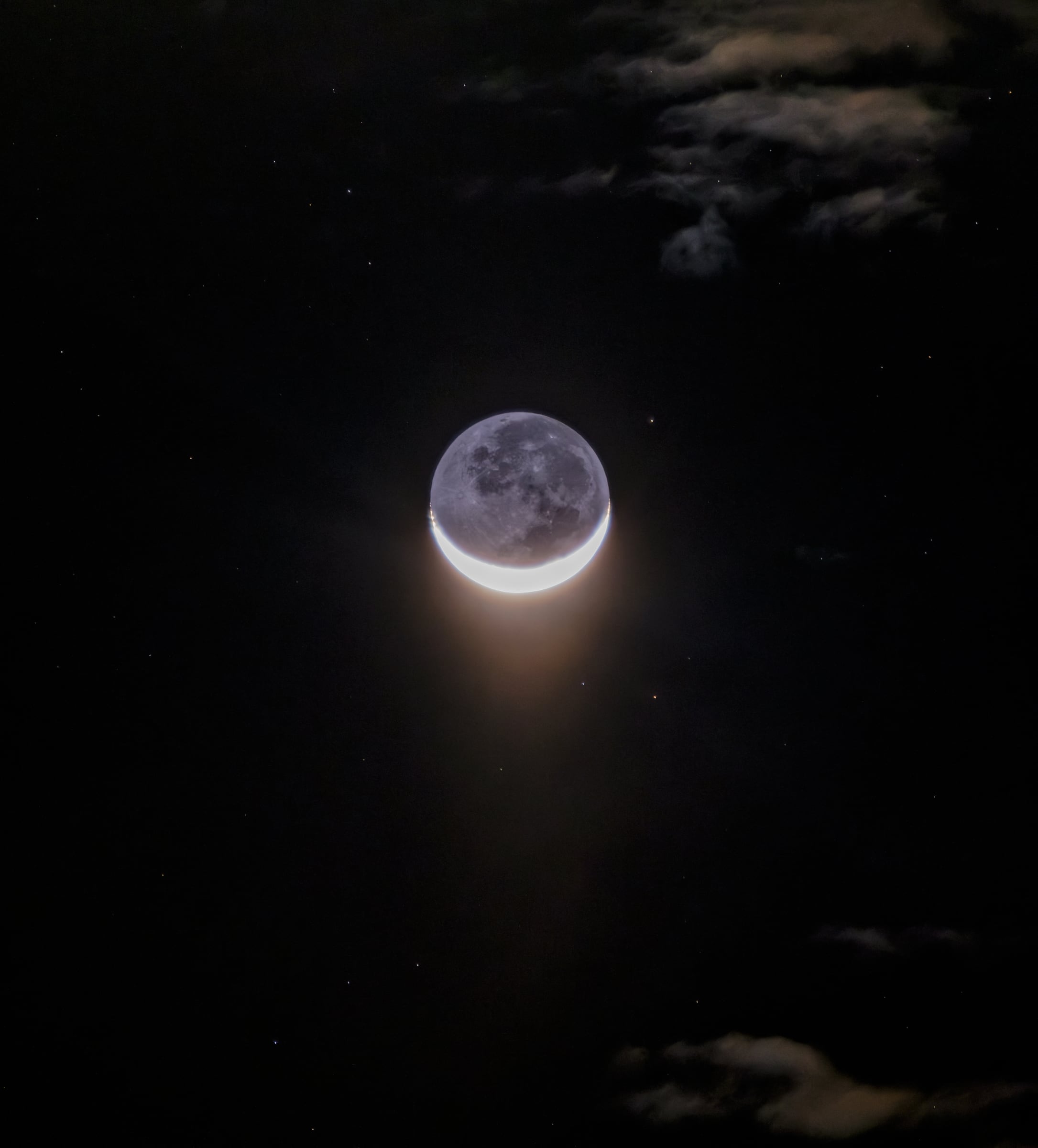 Solo una fina porción de la Luna recibe luz directa del Sol. El resto del disco se distingue gracias a la luz cenicienta, la luz solar que la Tierra refleja hacia la Luna, explicada por Leonardo da Vinci hace cinco siglos. En las puntas del creciente asoman pequeños destellos sueltos: cimas y bordes de cráter todavía iluminados mientras el terreno que los rodea ya está en sombra.